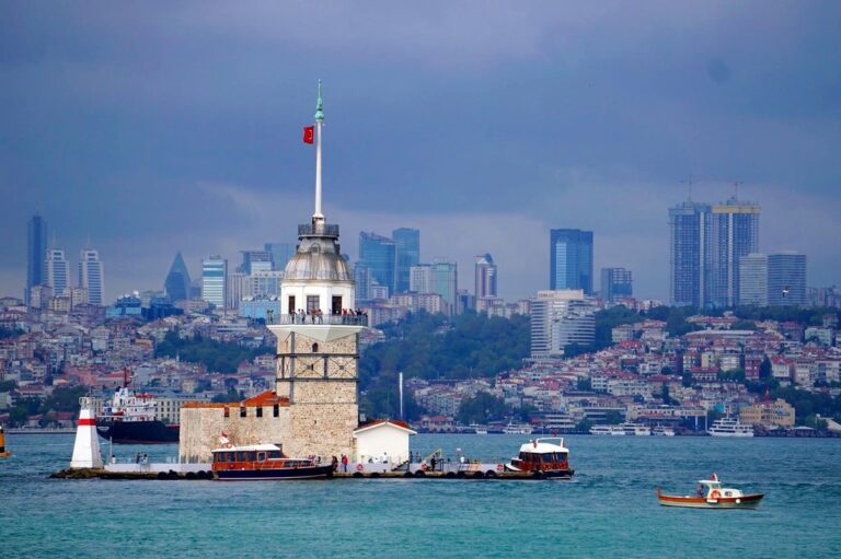 Distant view of the historical protected Meydan Tower at mid the bosporus water with the view of the city buildings behind the tower and the Turkish flag on top of it, in Istanbul, Turkey